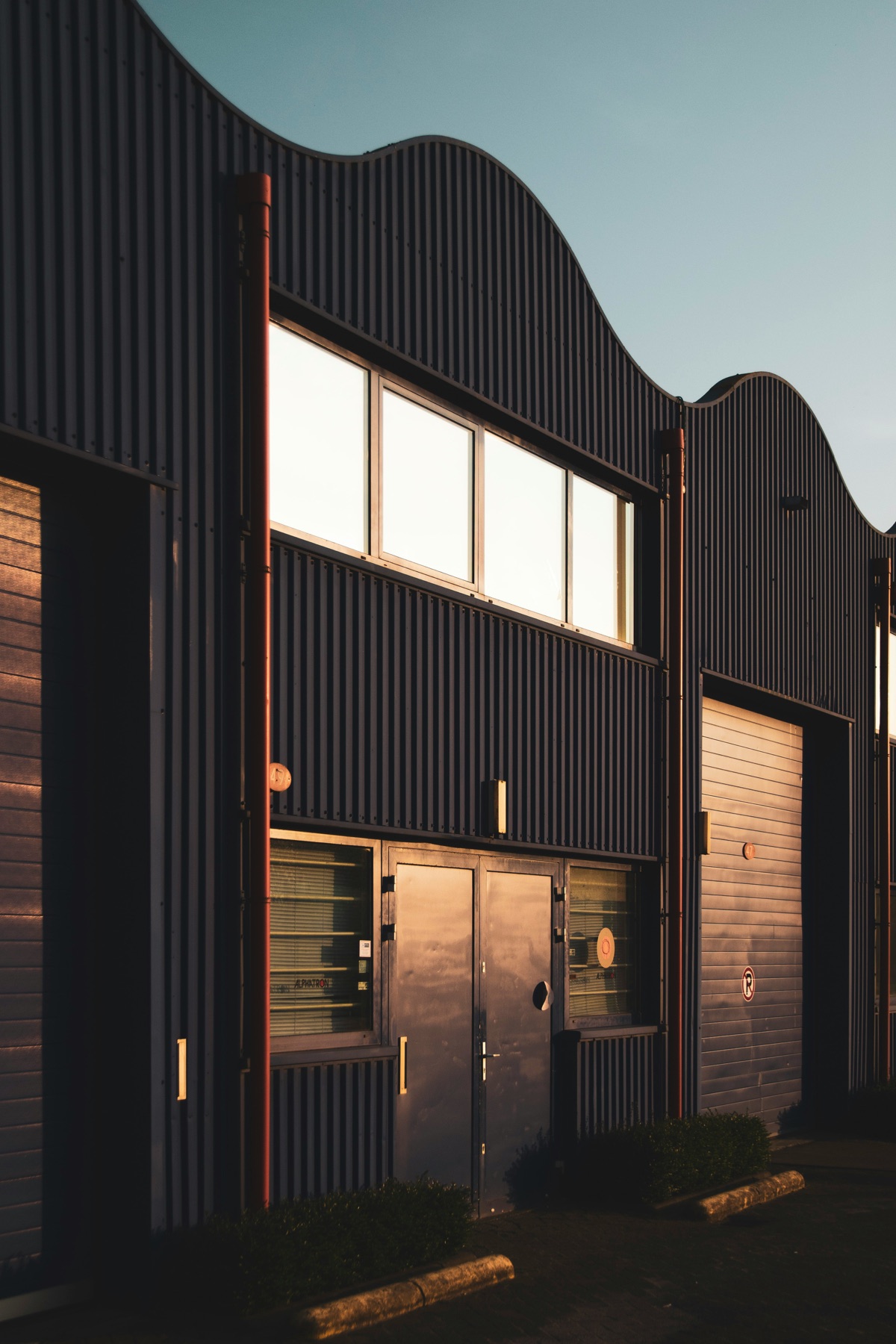 VS Projektai production facility exterior in Lentvaris, dark corrugated cladding with curved roofline